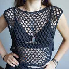 a woman with her hands on her hips wearing a crochet top and earrings