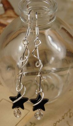 two black stars dangling from silver earwires on a clear glass bottle with writing paper in the background