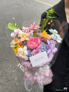 a woman holding a bouquet of flowers on the street in front of her face and wearing a black blazer