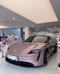 a pink sports car parked in a showroom with flowers on the floor and behind it