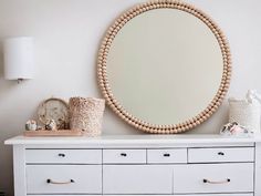 a white dresser topped with lots of drawers and a round mirror on top of it