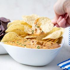 a person dipping tortilla chips into a white bowl