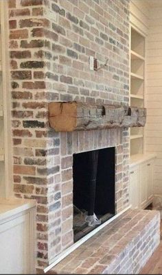 an empty living room with a brick fireplace and built - in shelving units on either side