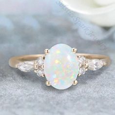 a white opal and diamond ring with three stones on the side, sitting on a table