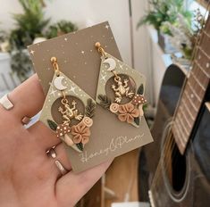 a pair of earrings with deer and flowers on them sitting in front of a guitar