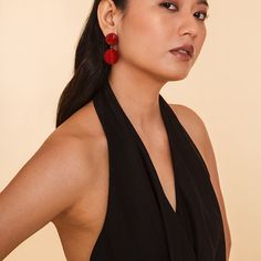 a woman in a black dress with red earrings on her head and one hand on her hip