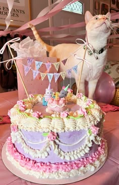 a cat standing next to a cake on top of a pink table cloth covered table