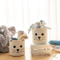 three baskets with animals on them sitting on a table next to pillows and stuffed animals