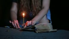 a woman holding a lit candle over an open book