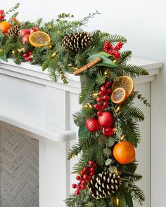 a christmas garland with oranges, pine cones and other decorations hanging on a fireplace mantel