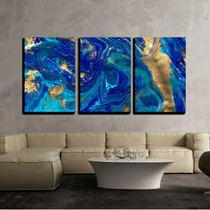 three abstract paintings in blue and gold on a wall above a white couch with a coffee table