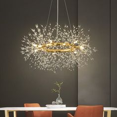 a chandelier hanging over a dining room table with orange chairs and a vase