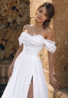 a woman in a white dress standing next to a stone wall and posing for the camera