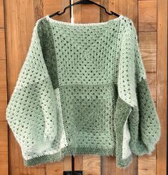 a green knitted sweater hanging on a hanger in front of a wooden door