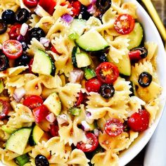 pasta salad with cucumbers, tomatoes, olives and other vegetables in a white bowl