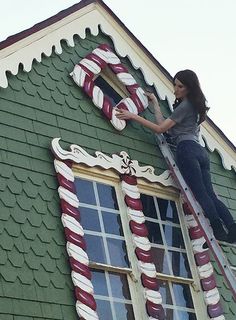 a woman on a ladder painting the side of a green house with candy canes