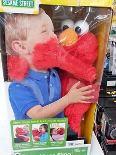 a young boy holding a red stuffed animal in front of a store display with other items