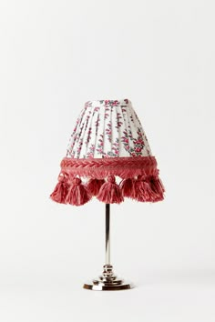 a red and white lamp shade on a metal base with pink tasselled trim