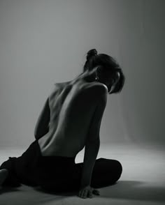 black and white photograph of a naked woman sitting on the floor with her back to the camera