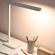 a white desk lamp sitting on top of a table next to a cup filled with pencils