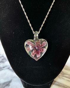 a heart shaped glass pendant with pink flowers on it sitting on a mannequin