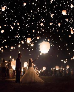 a bride and groom are holding lanterns in the air at night with people looking on