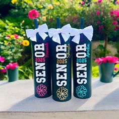 three black bottles with white bows are sitting on a table in front of some flowers