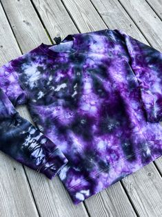 a purple and black tie - dyed sweatshirt sitting on top of a wooden floor