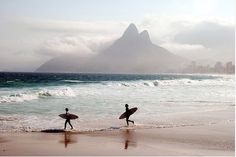 two surfers are walking on the beach with their surfboards in front of them