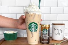 a hand holding a starbucks drink with whipped cream on top and two other drinks next to it