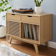 a record player sitting on top of a wooden cabinet next to a potted plant