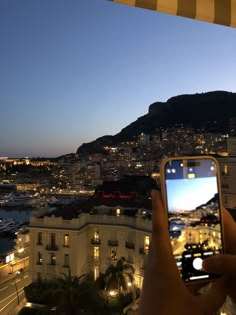 a person holding up a cell phone in front of a cityscape at night