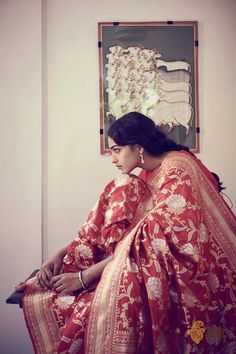 a woman in a red and gold sari sitting on a bench with her hand on her hip