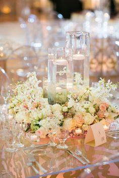 the table is set with clear glassware, flowers and candles on it's centerpiece