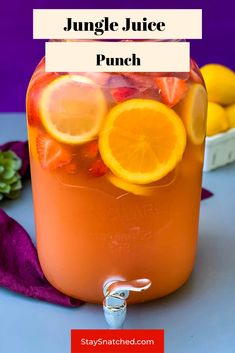 a jar filled with orange juice and sliced lemons on top of a table next to purple cloth