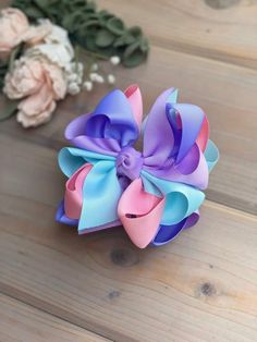 a pink, blue and purple hair bow sitting on top of a wooden table next to flowers