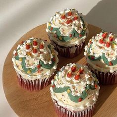 four cupcakes with white frosting and sprinkles on a wooden plate