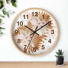 a clock with flowers on it next to a potted plant and a white wall