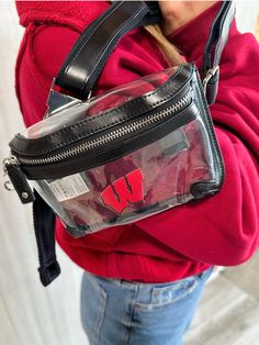 Go hands free with this trending Wisconsin Badgers belt bag design! The belt bag features a clear PVC body with gold hardware and PU Leather accents. The main zippered storage compartment is perfectly sized to fit your cell phone, cash and credit cards, lip gloss, keys, or any small essentials. Secure the belt bag easily around your waist with the cotton webbed and PU leather accented adjustable strap and metal side release buckle. Wear around your waist through your belt loops, sans the belt lo Trendy Crossbody Phone Bag With Zipper Pouch, Trendy Belt Bag With Zipper Closure For On-the-go, Trendy School Belt Bag With Zipper Pocket, Trendy Rectangular Belt Bag With Zipper, Trendy School Belt Bag With Cell Phone Pocket, Trendy School Belt Bag With Zipper Closure, Trendy Belt Bag With Removable Pouch For School, Trendy Belt Bag With Zipper For On-the-go, Trendy Clear Bags With Zipper Pouch