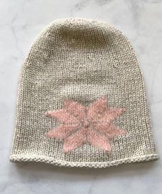 a knitted beanie with pink flowers on the front and bottom, sitting on a marble surface