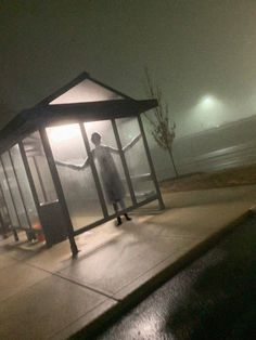 a man standing in front of a bus stop on a foggy night with no one around