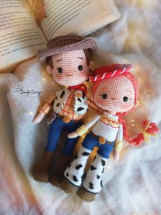 two small knitted dolls are sitting on a bed with an open book in the background