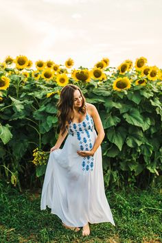 a pregnant woman standing in front of a field of sunflowers