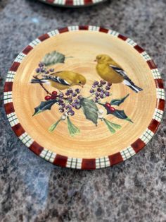 two plates with birds painted on them sitting on a marble counter top next to each other