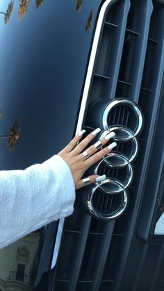 a woman's hand on the front grille of a black car with four rings