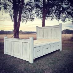 a white bed sitting in the middle of a field next to two trees and a fence