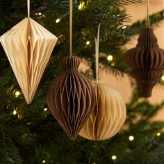 three brown origami ornaments hanging from a christmas tree with lights in the background