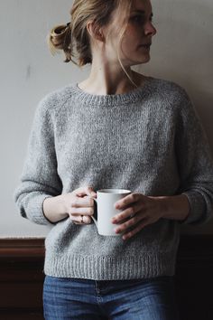 a woman is holding a coffee cup in her hands and looking off into the distance