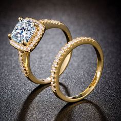 two gold wedding rings sitting on top of a black surface with a diamond in the middle