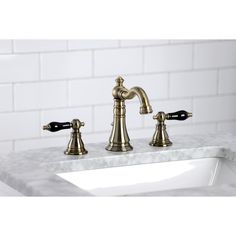 a bathroom sink with two faucets and marble counter top in front of a white brick wall